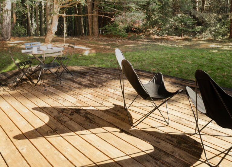 Paradiso - outdoor wooden deck with small dining table and lounge chairs looking to forest